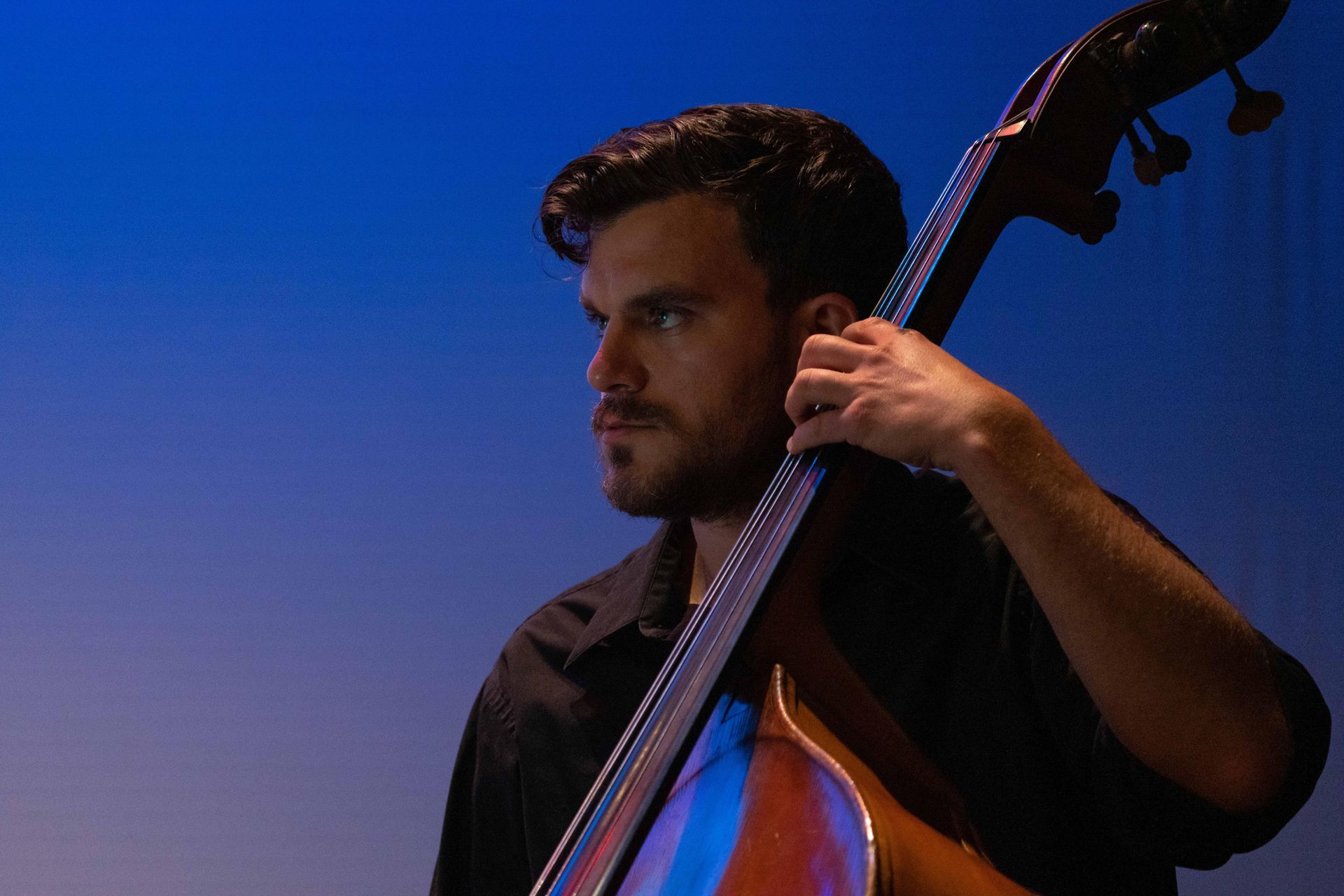Man holding an upright bass on a blue-lit stage, looking to the side