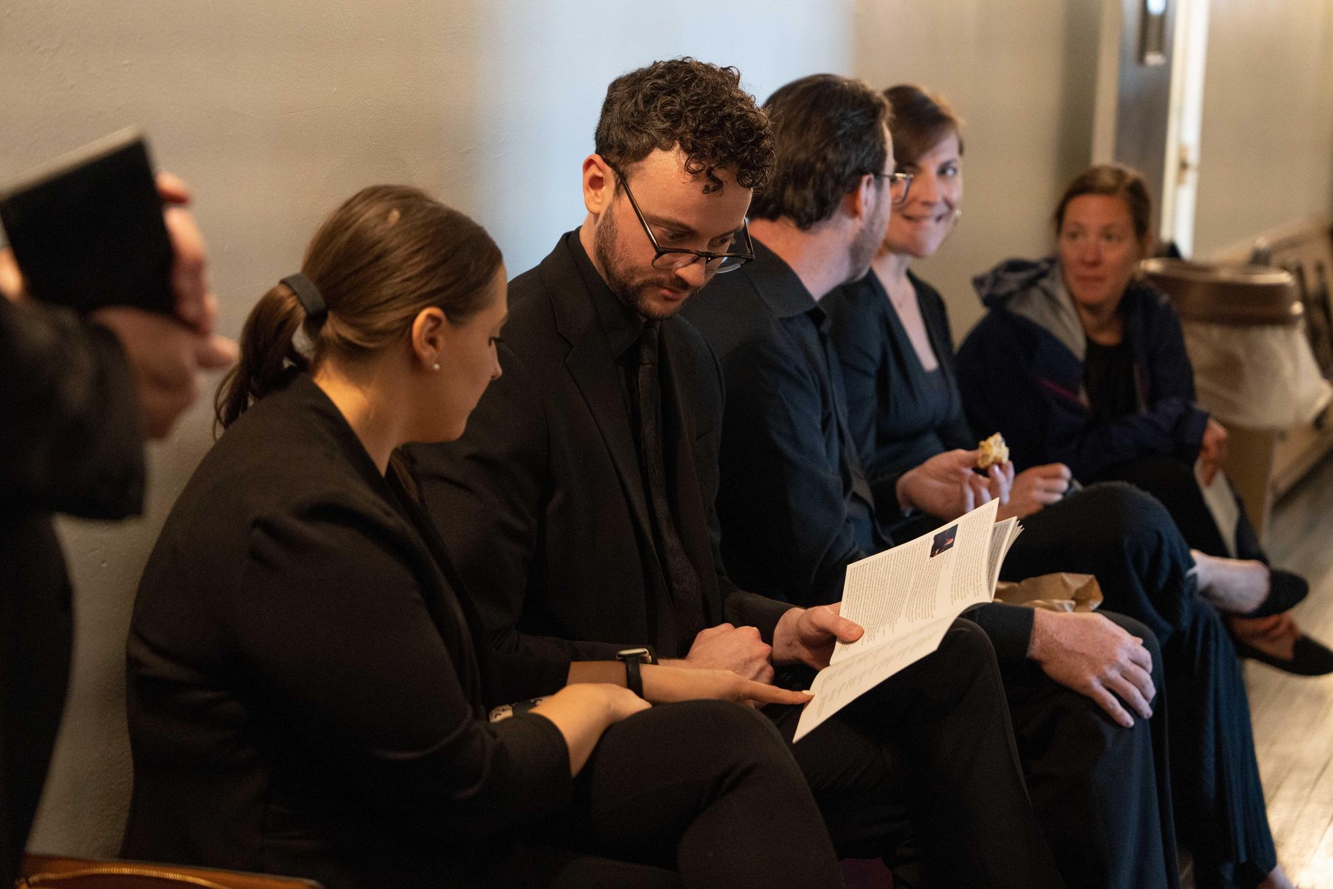People seated in a row reading papers at a formal indoor event