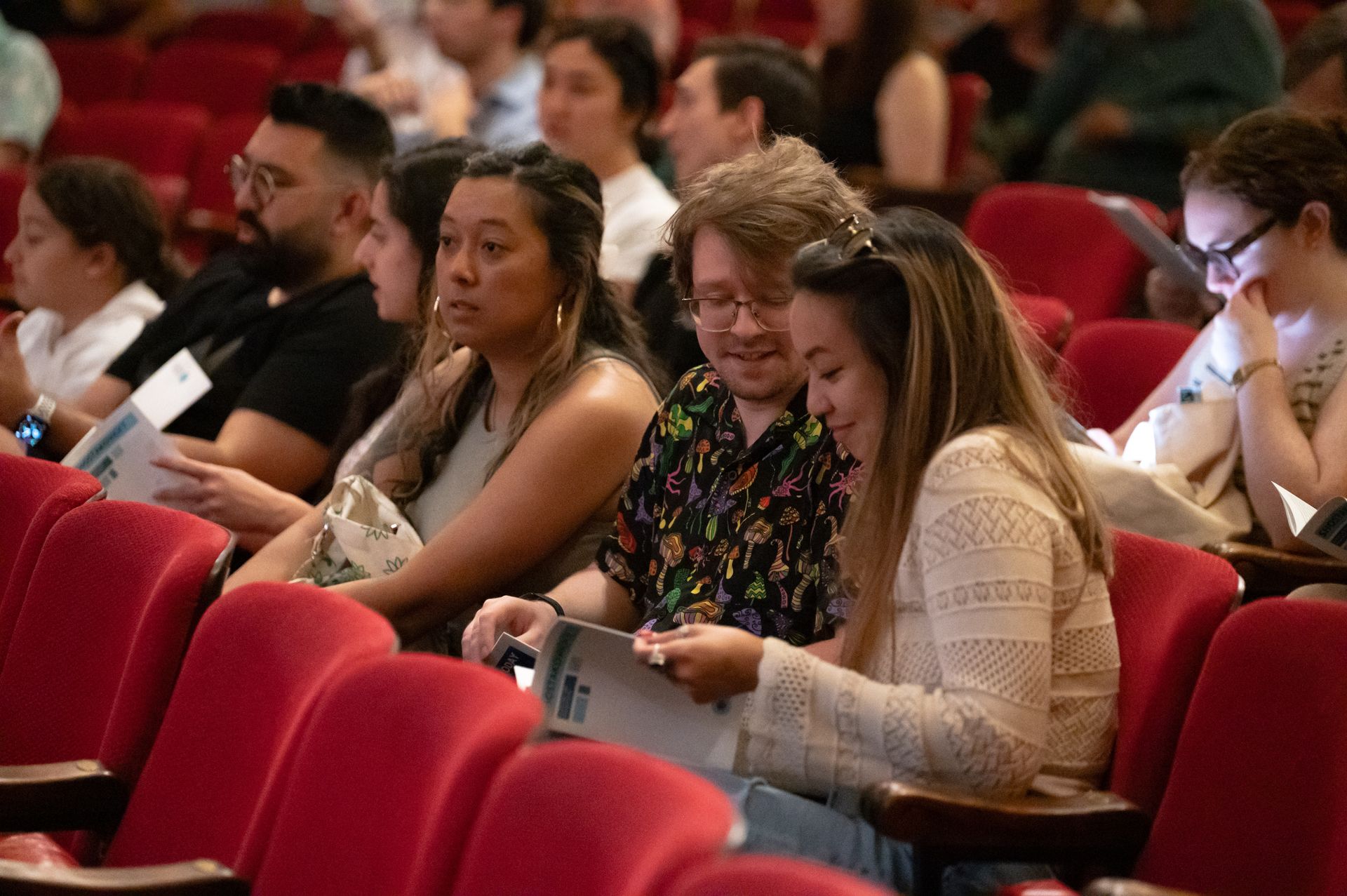 Audience seated in a theater, with two people in the foreground looking at a program.
