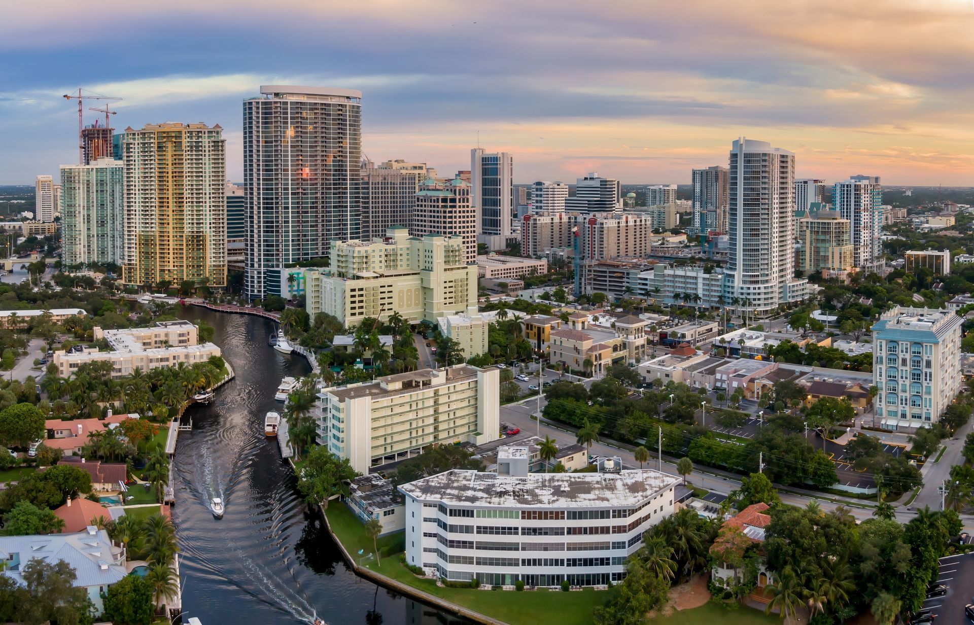 City skyline at sunset with high-rise buildings, a winding road, and lush greenery in the foreground
