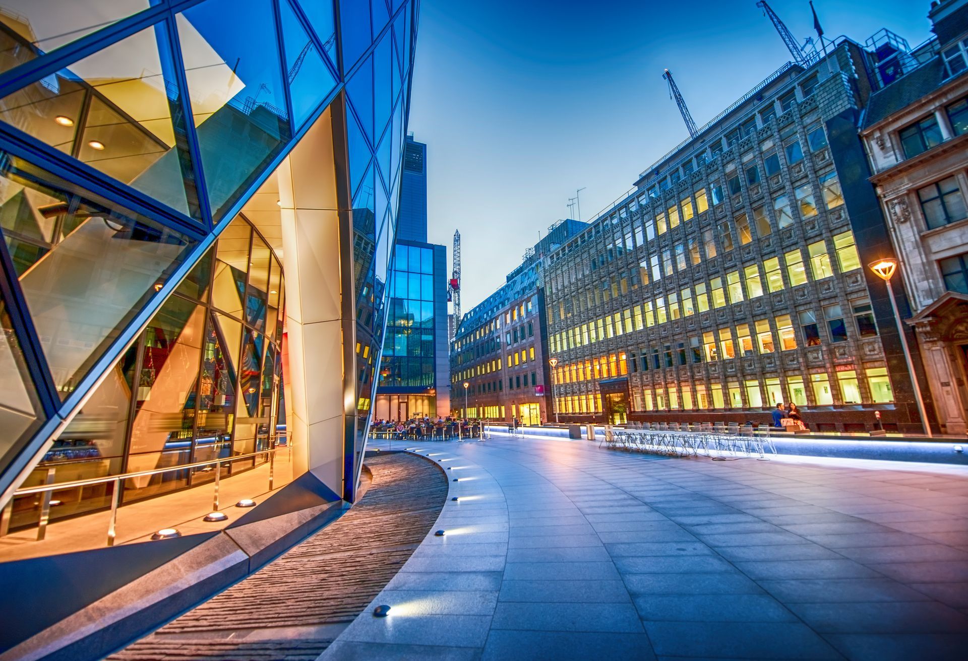 Modern city street at dusk with illuminated glass buildings and a curved pedestrian walkway