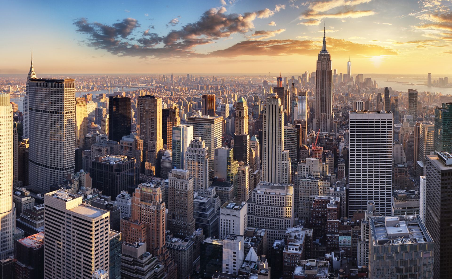 New York City skyline at sunset with the Empire State Building centered among tall skyscrapers.