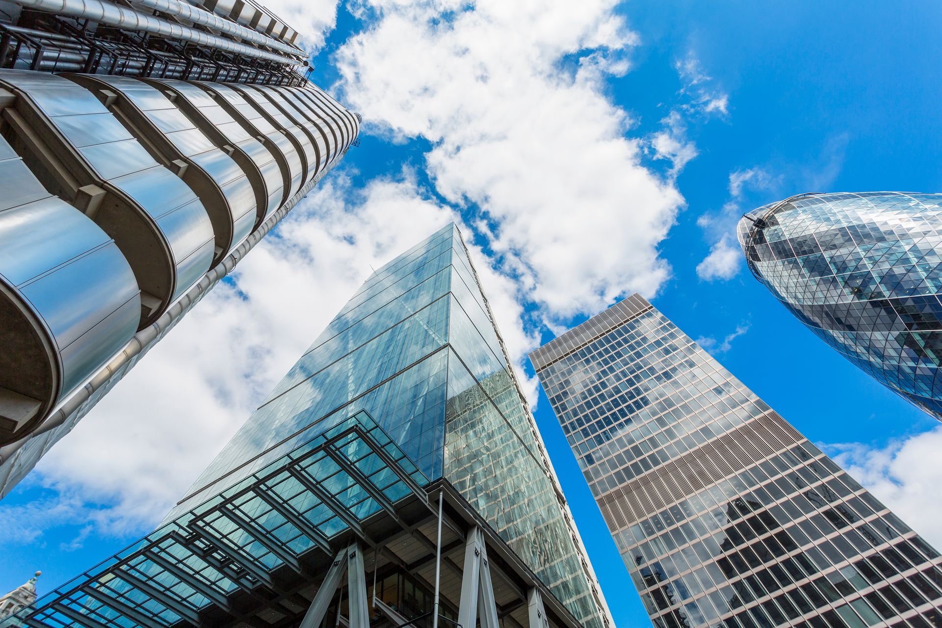 Skyscrapers with glass facades viewed from below against a bright blue sky and clouds