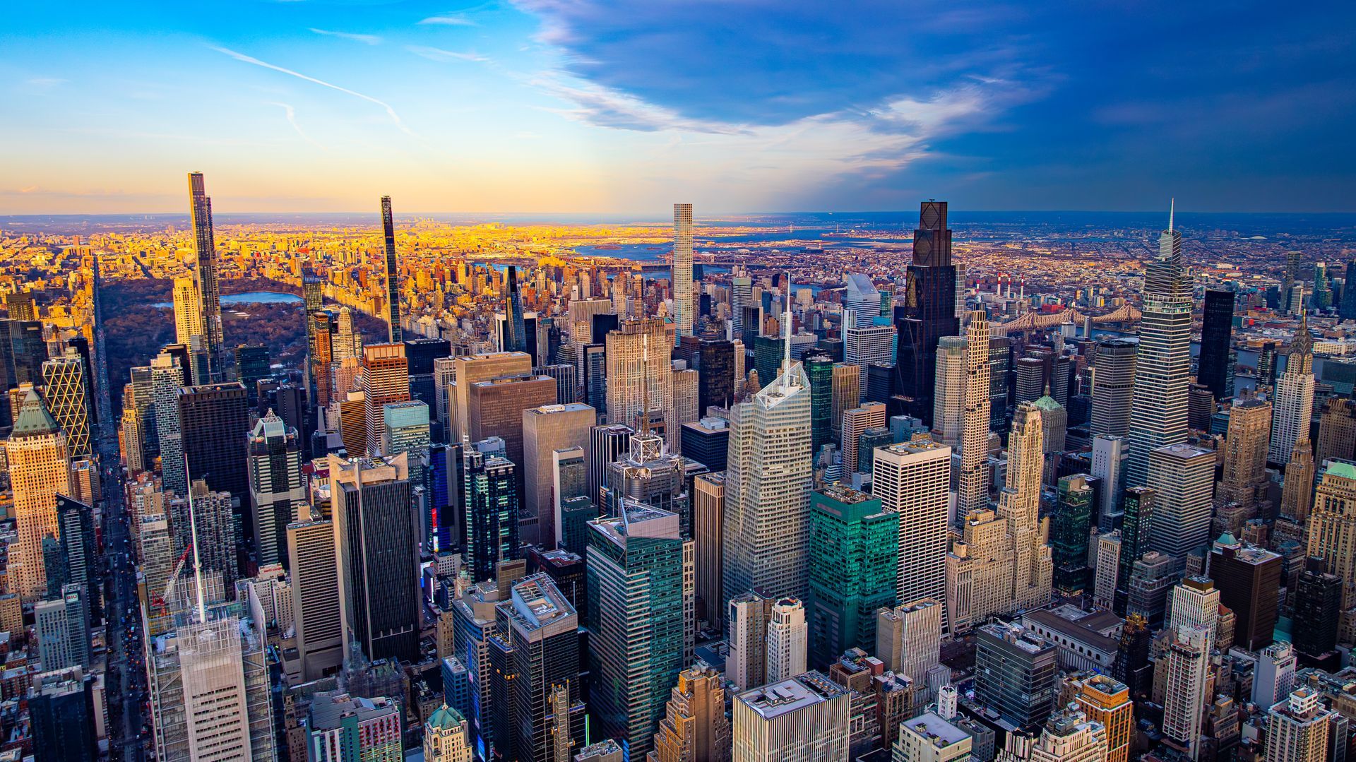 Aerial view of a dense city skyline at sunset with tall skyscrapers and warm golden light.