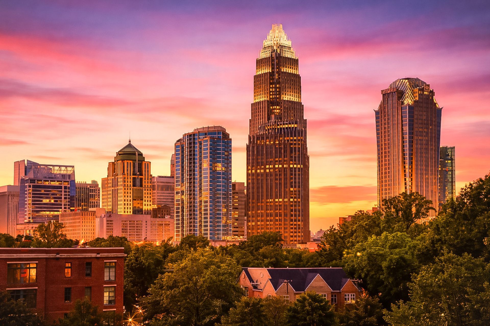 Charlotte skyline at sunset with glowing skyscrapers under a pink-orange sky