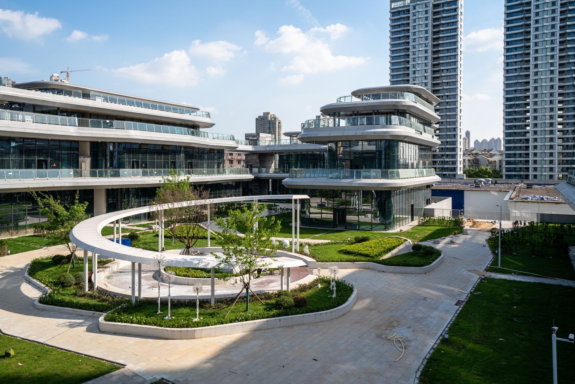Modern terraced buildings and landscaped courtyard with circular walkway, under a blue sky.
