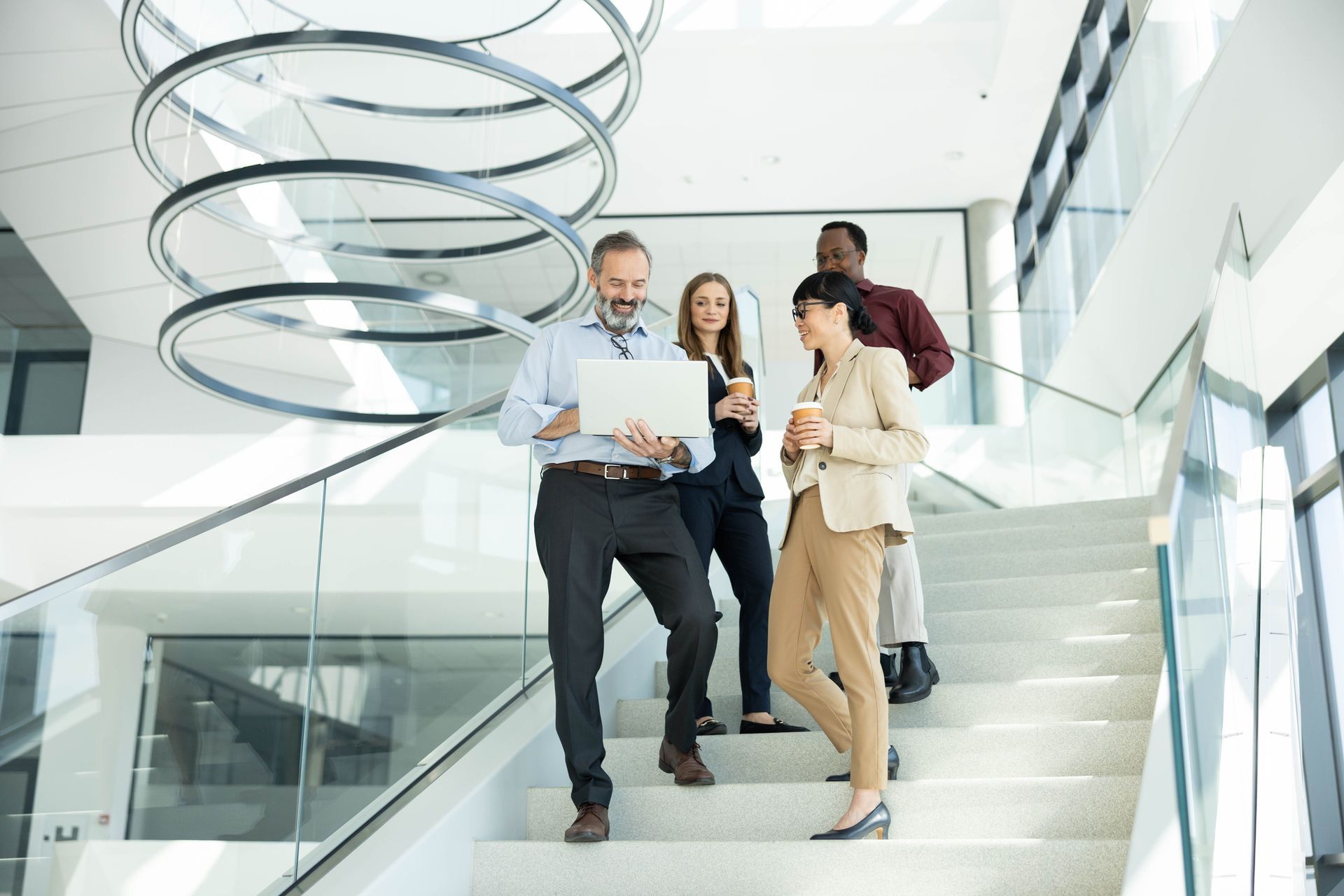 Three people walking down stairs in a bright modern office, looking at papers and discussing.