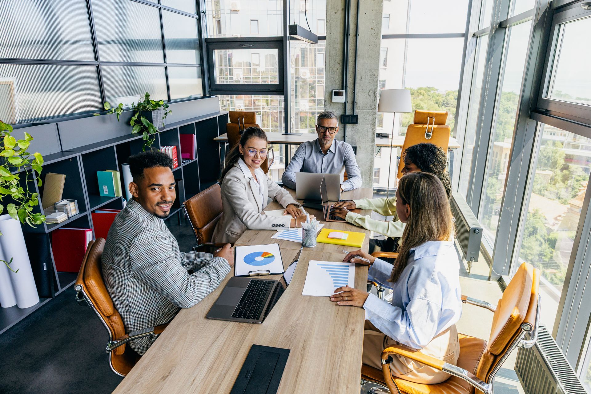 Four coworkers meeting around a laptop at a wooden table in a bright office