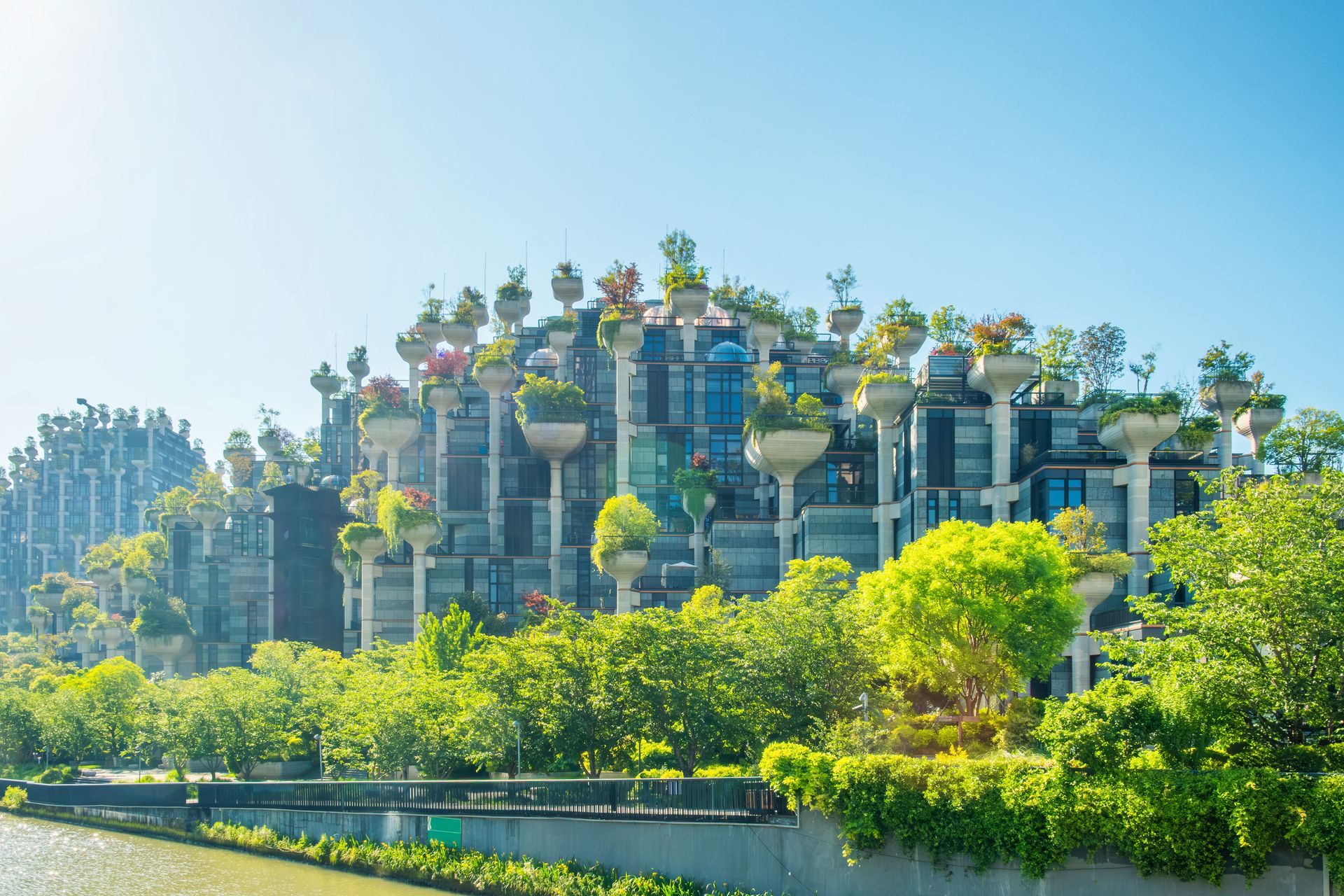 Lush green hillside with terraced futuristic towers covered in plants under a bright blue sky