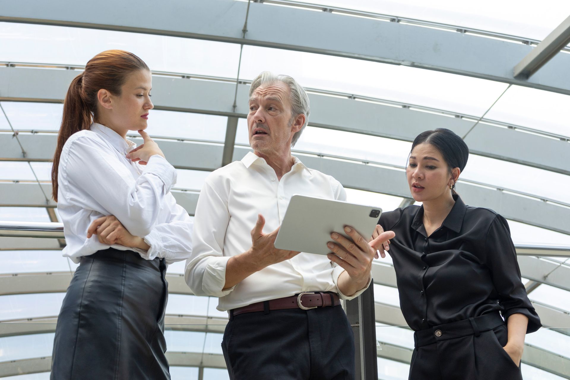 Three coworkers in business attire discussing a document in a bright modern office.