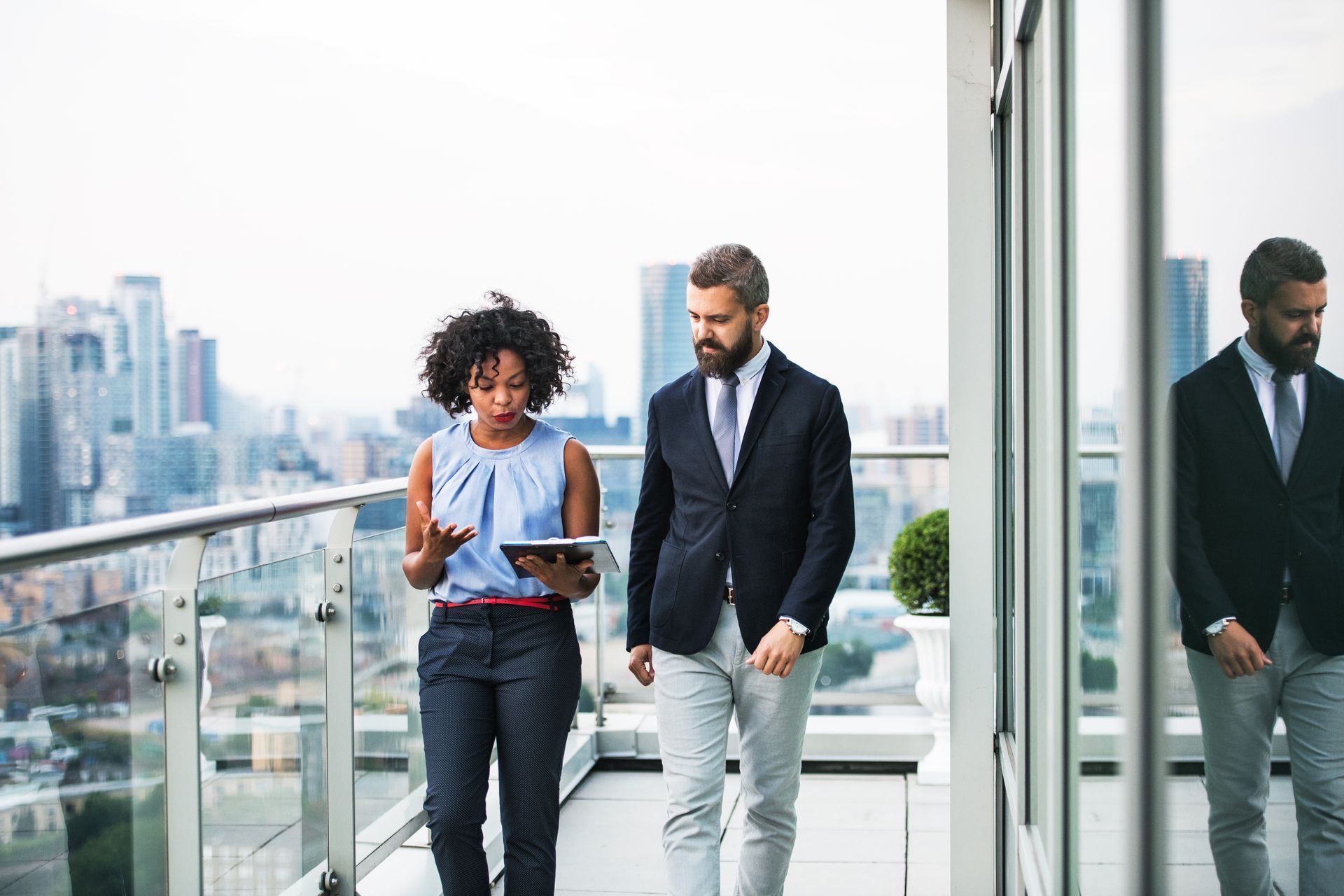 Two professionals walking and discussing on a rooftop terrace with a city skyline in the background