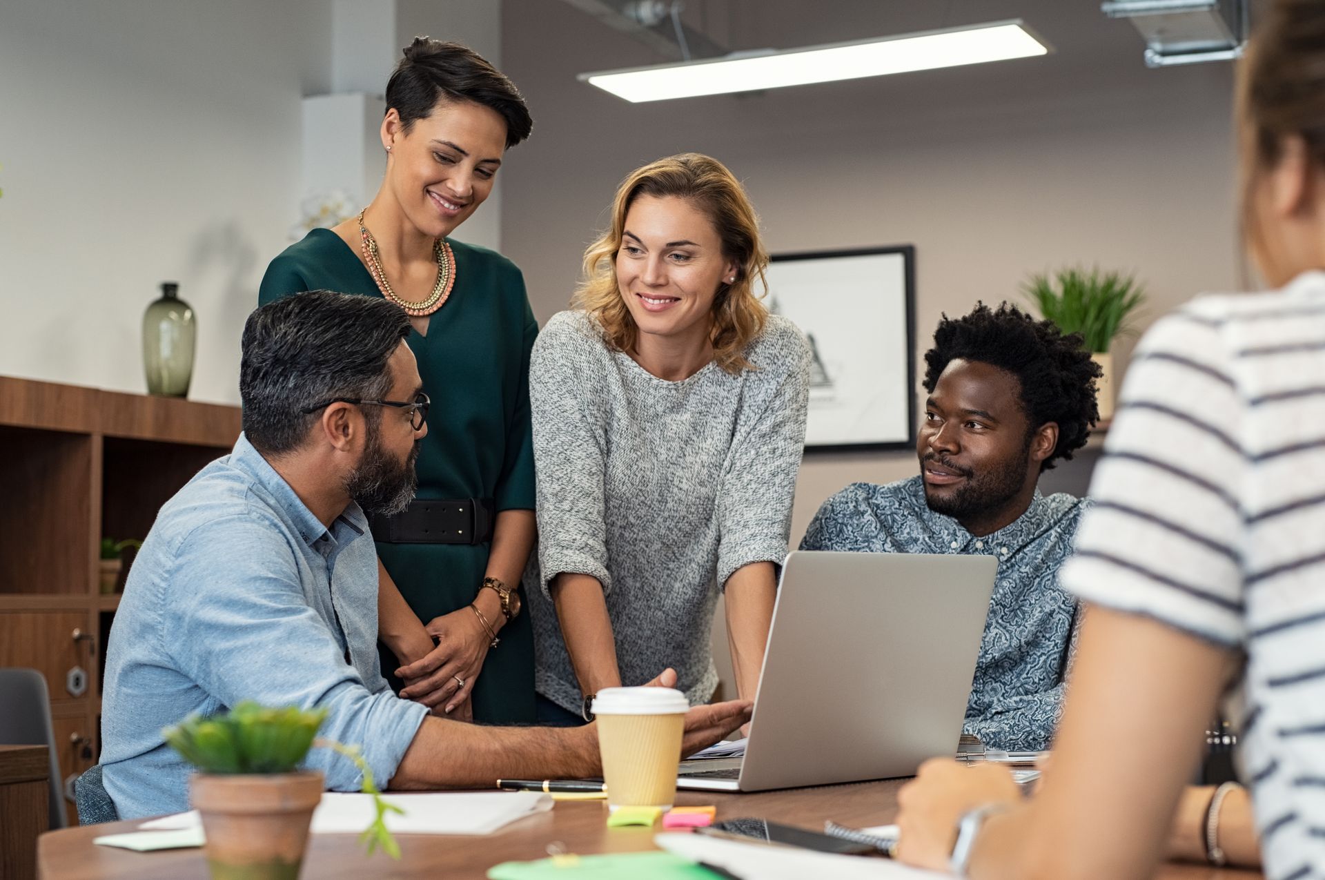 Team meeting around a laptop in a bright office, with five people discussing together.