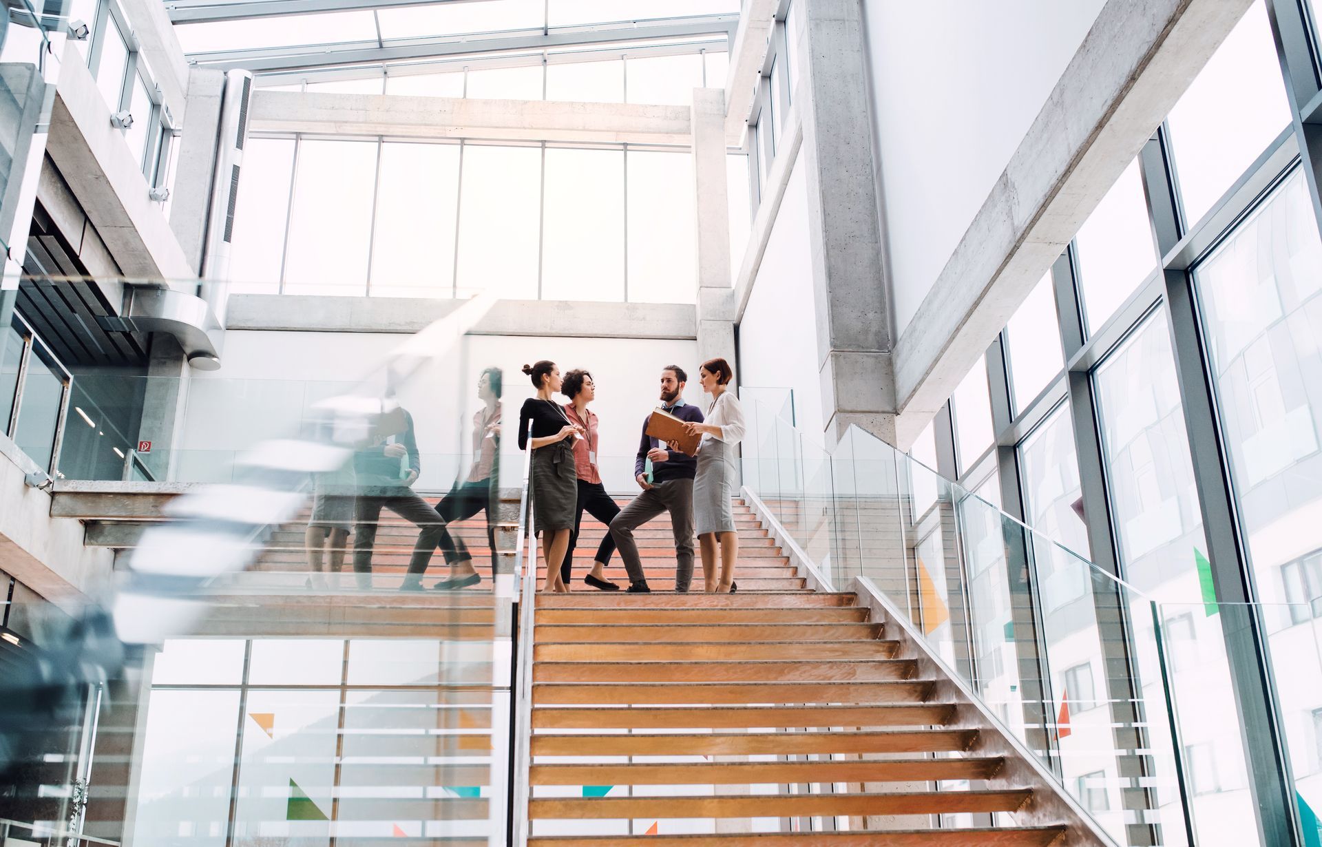 People standing on a glass staircase in a bright modern office atrium