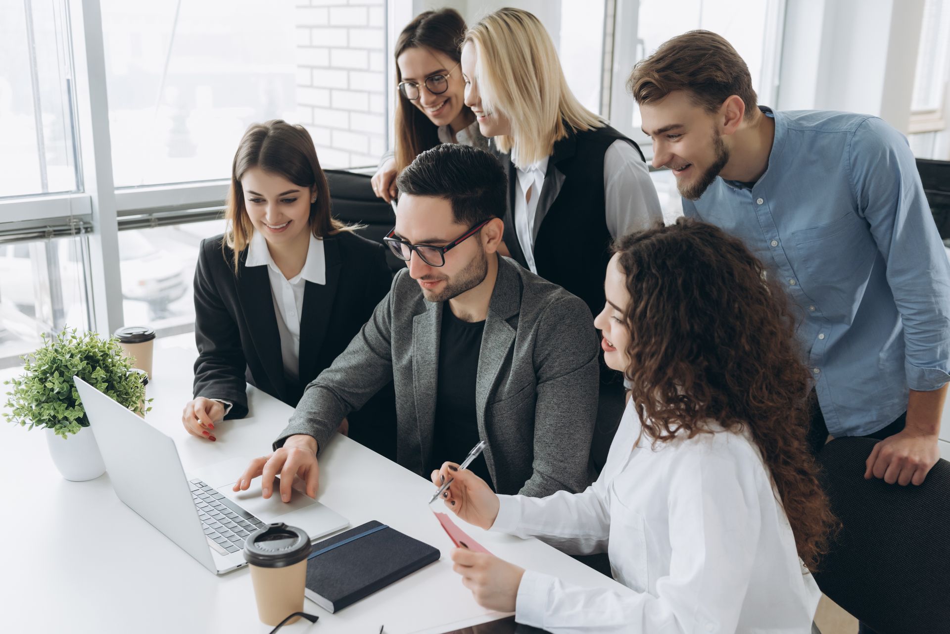 Team of coworkers gathered around a laptop in a bright office, collaborating and reviewing documents.