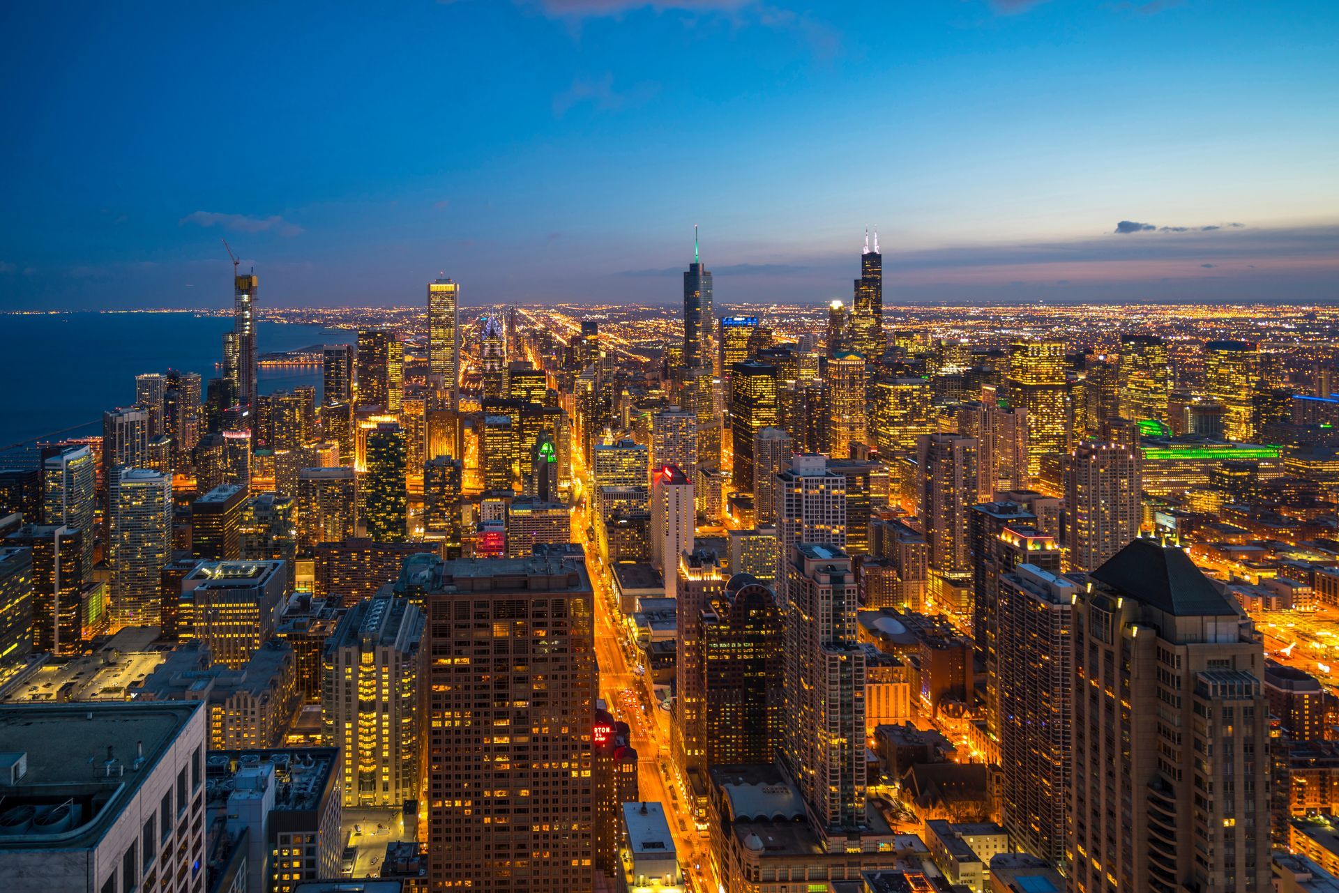 Chicago cityscape at dusk, illuminated buildings along a long street, Lake Michigan in background.