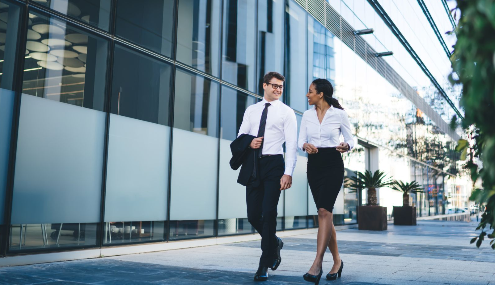 Two people in business attire walking and talking outside a modern building.