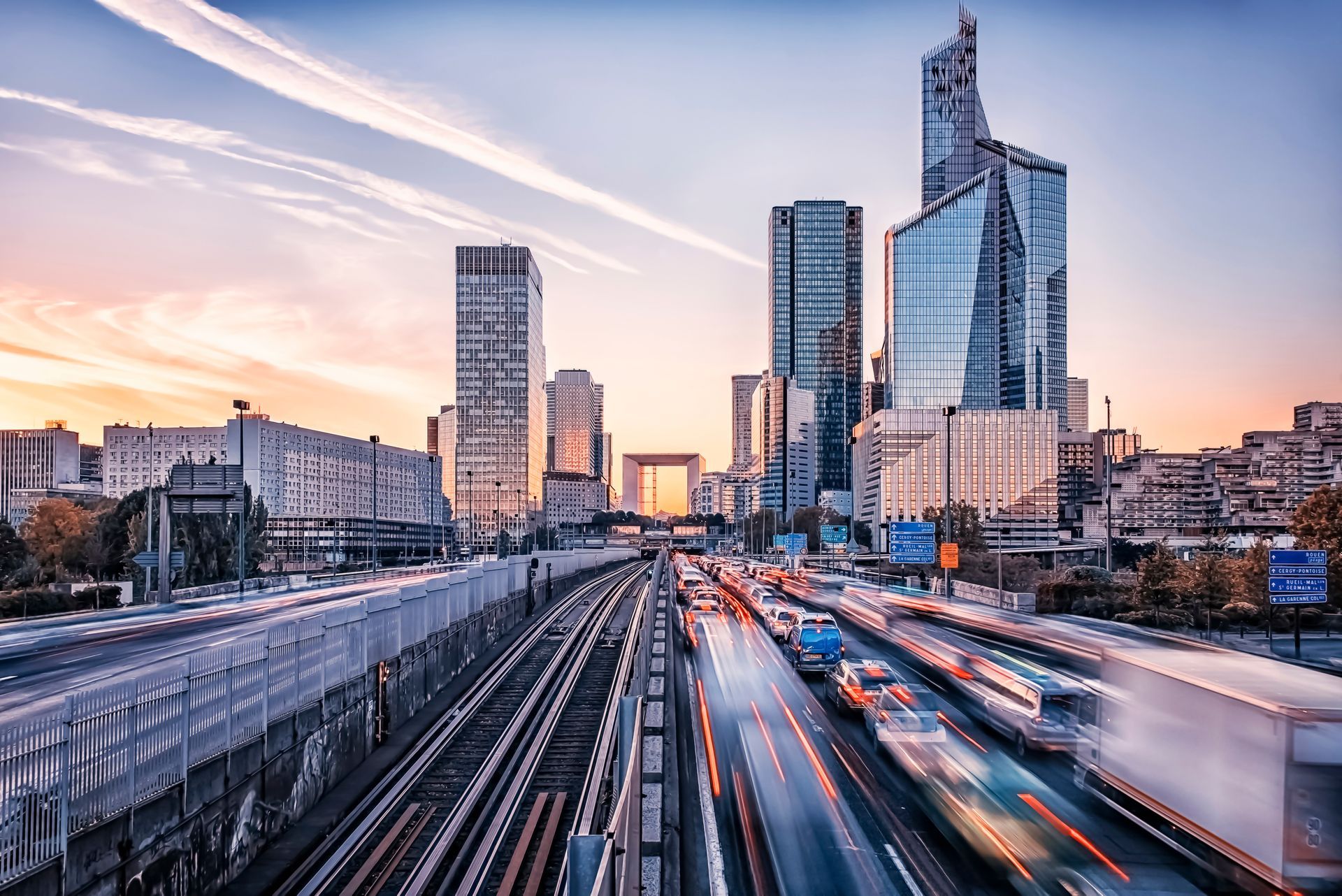 City skyline at sunset with light trails on a busy highway and modern glass towers