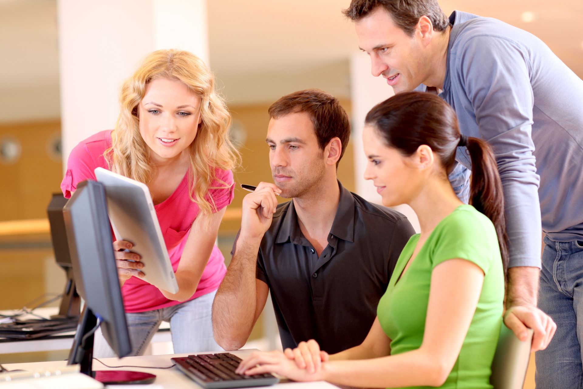 Four coworkers gathered around a desktop computer, reviewing something on the screen together.