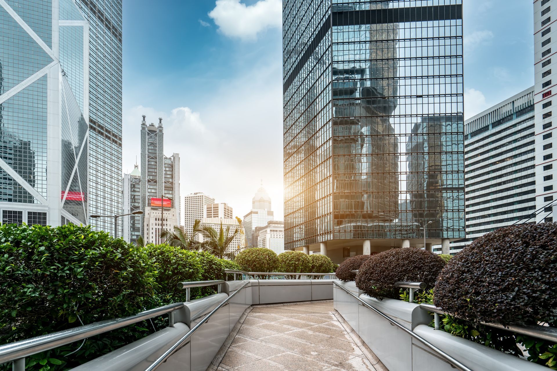 Modern city skyline with glass office towers and a landscaped walkway at sunset