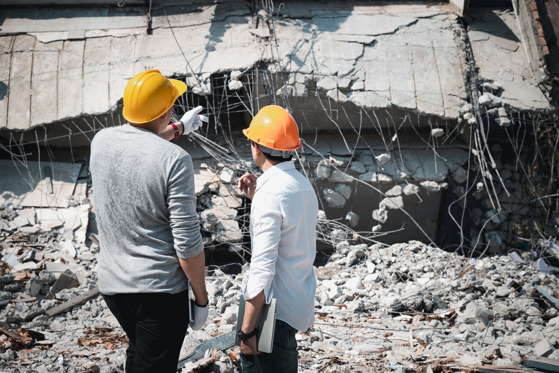Two men in hard hats survey a ruined building.