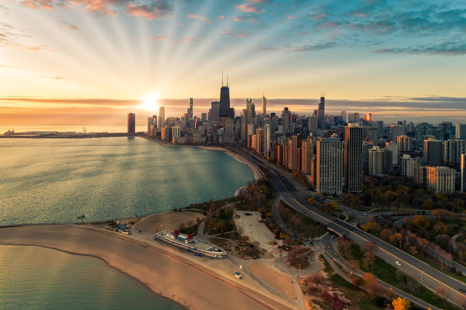 Sunset over a coastal city skyline, with beach, bay, and waterfront high-rises.