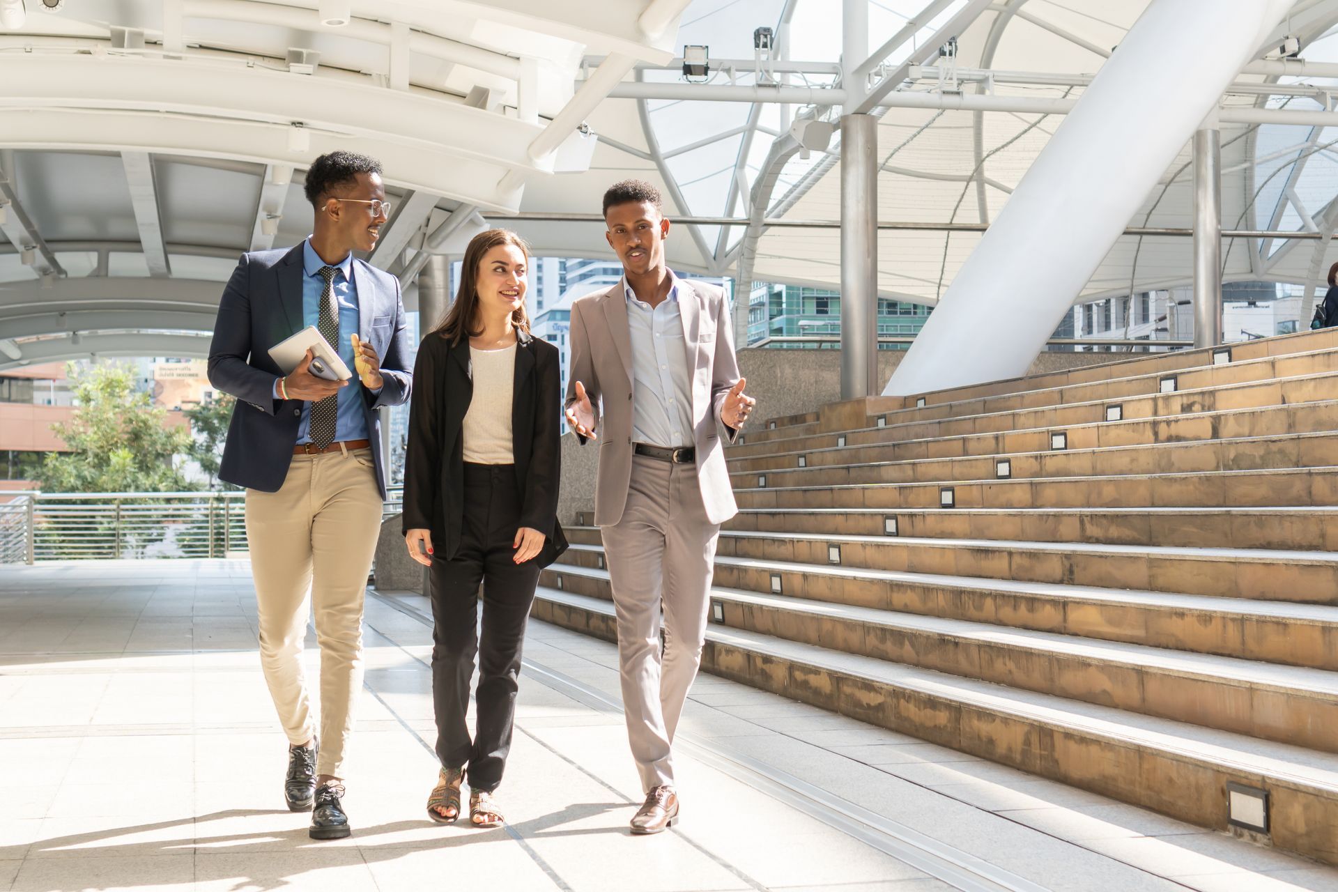 Three professionals walking beside modern outdoor stairs in a bright, covered walkway