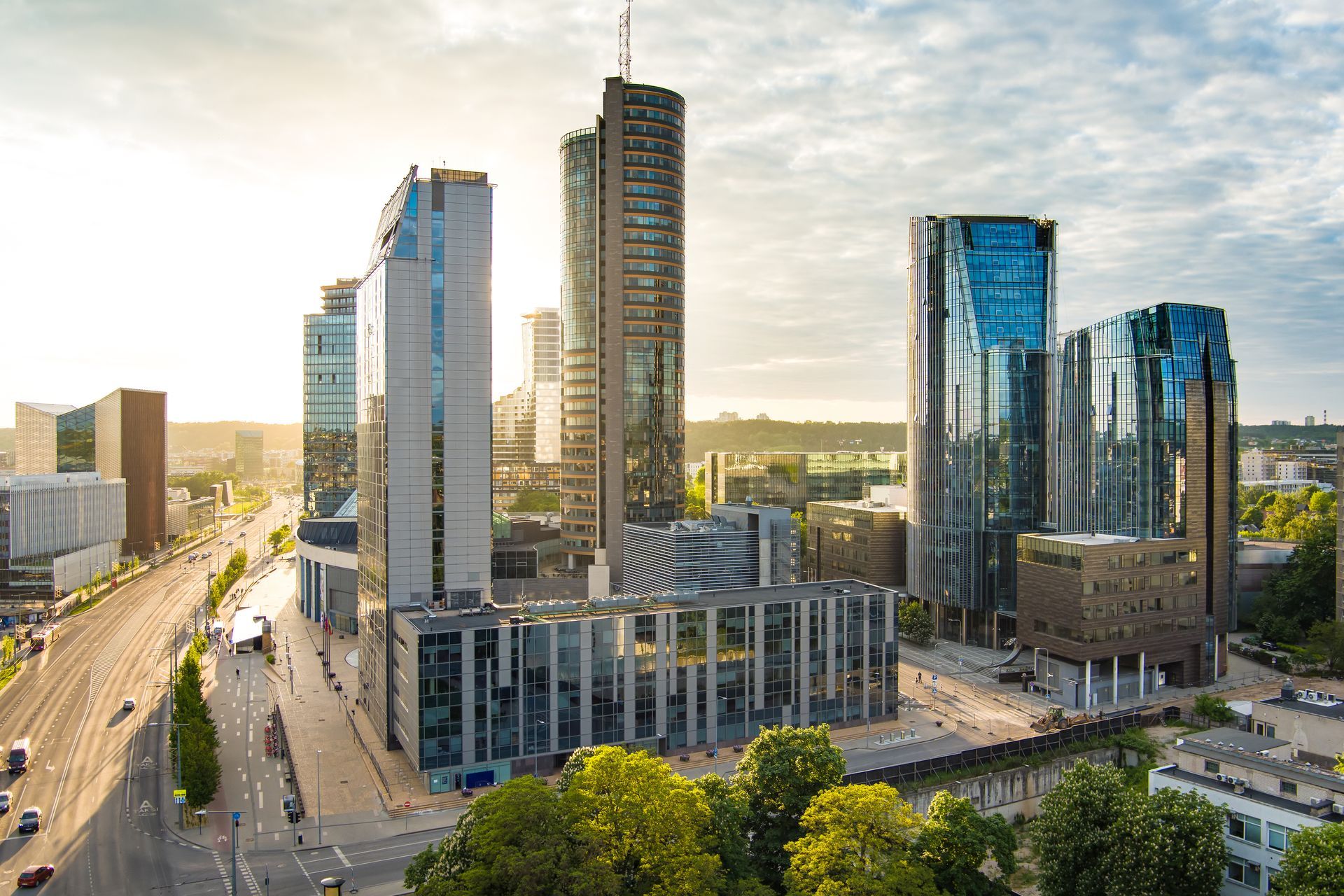 Modern city skyline with tall glass skyscrapers beside a sunlit street and bridge
