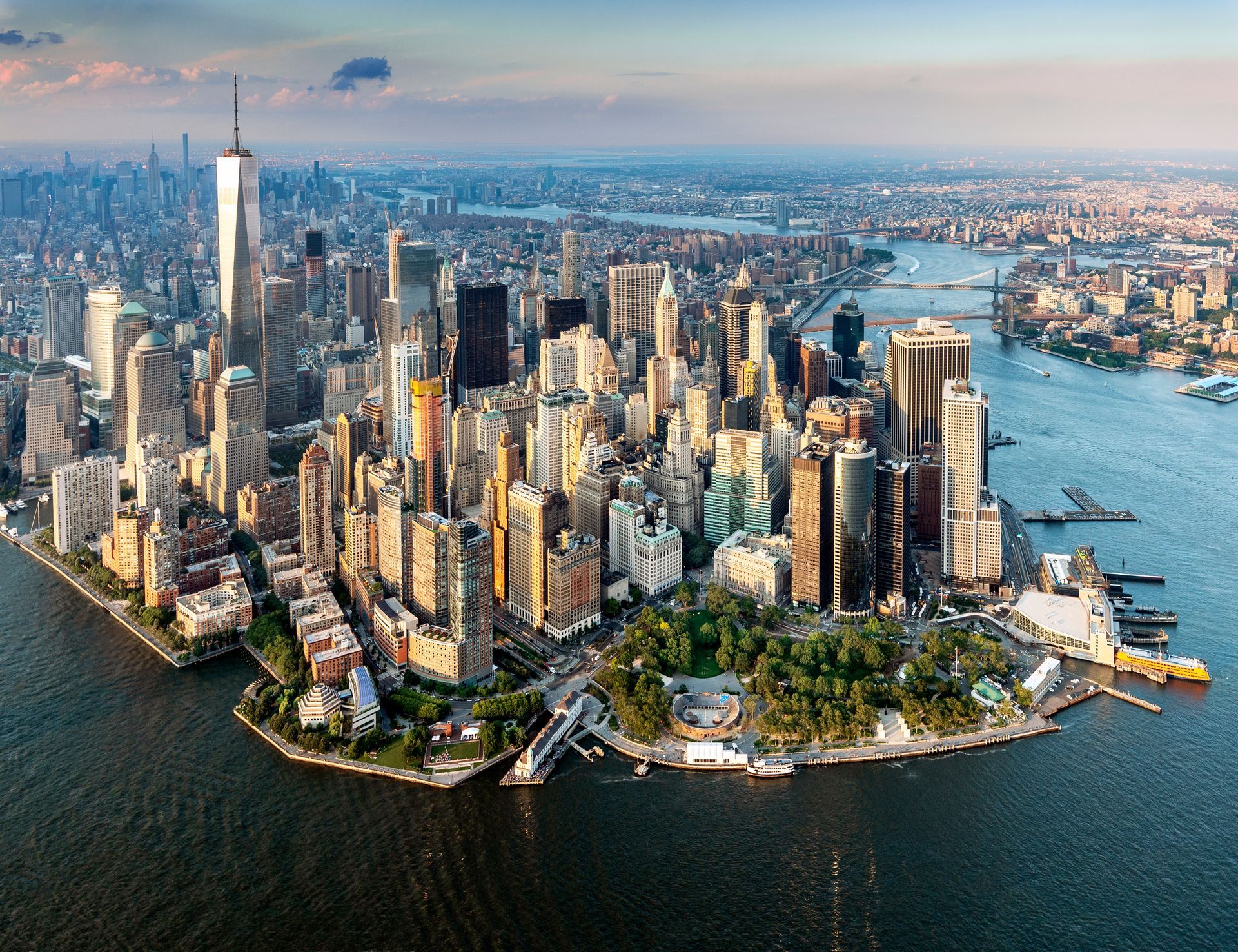 Aerial view of Lower Manhattan skyline with tall skyscrapers by the waterfront at sunset