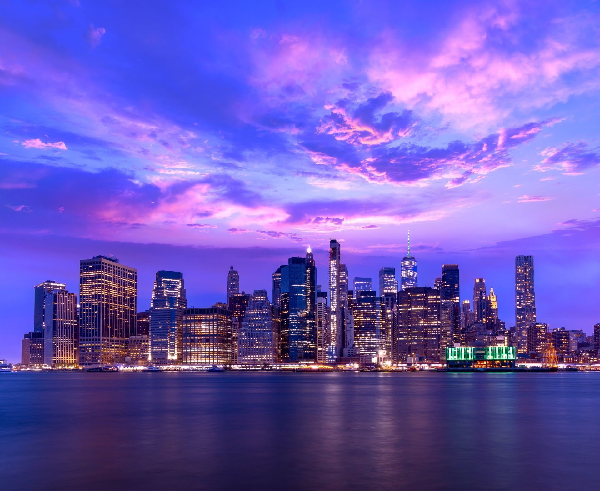 City skyline at dusk with purple clouds reflected on calm water