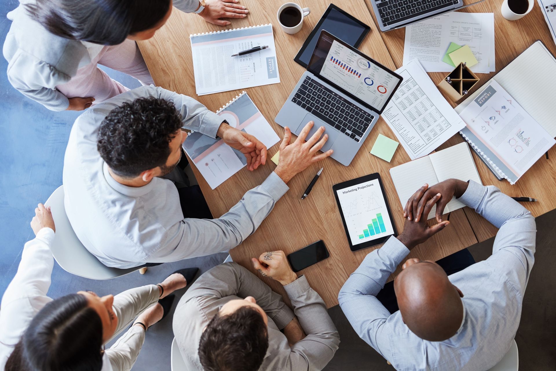 Team meeting around a table with laptops, notebooks, and charts, viewed from above