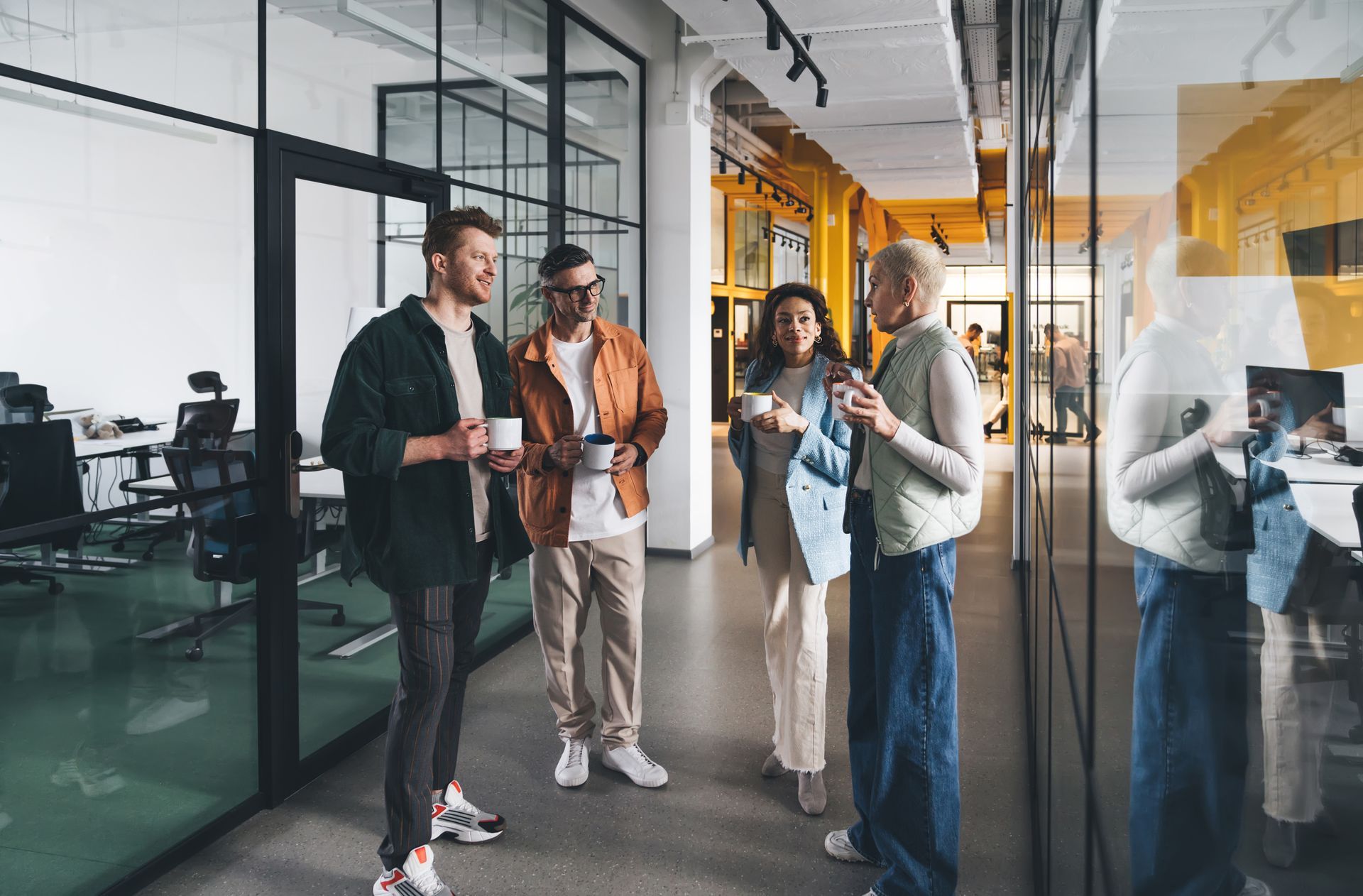 People talking in a modern office hallway with glass walls and desks in the background