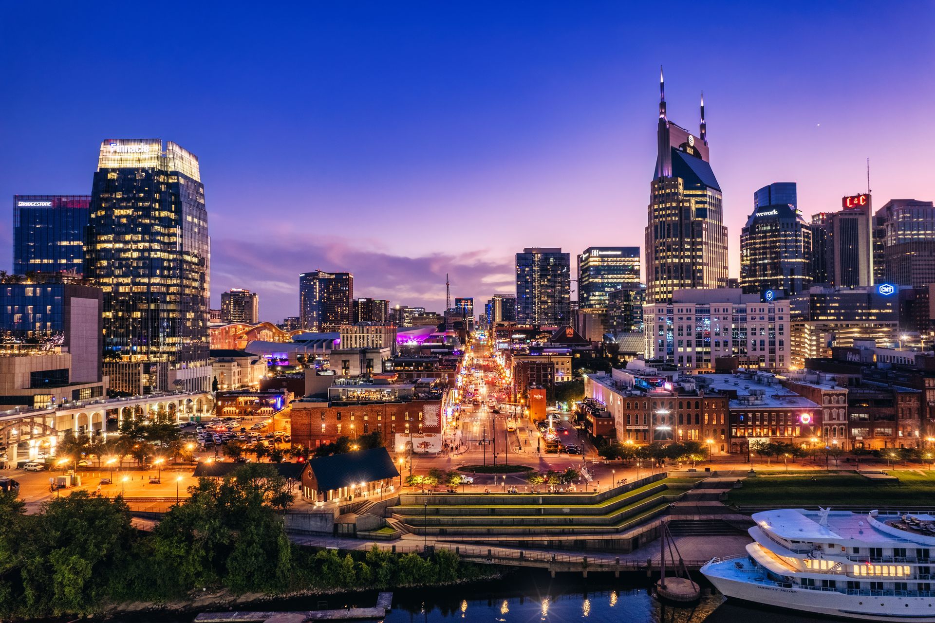City skyline at dusk with illuminated buildings and a lit waterfront promenade.