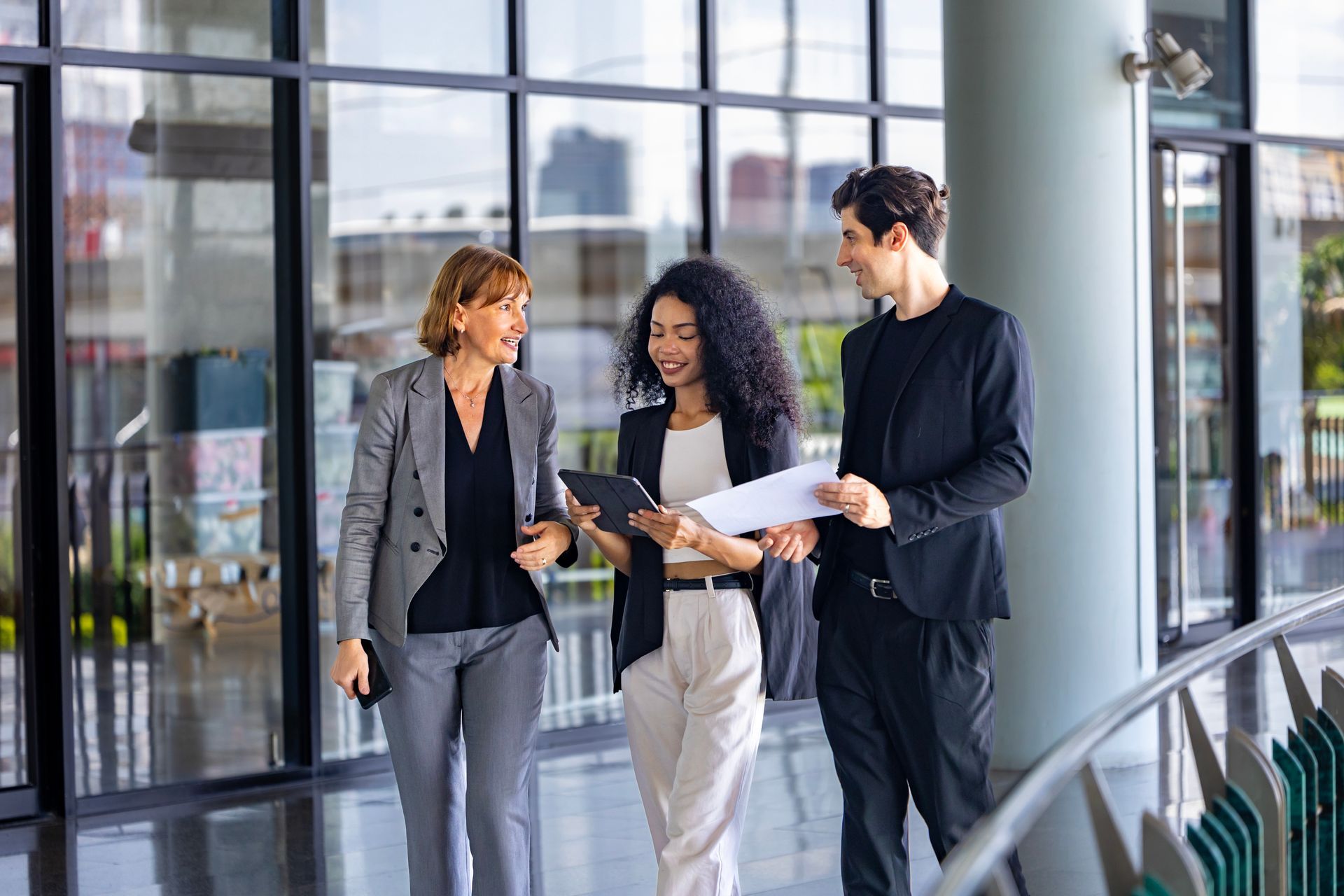 Three colleagues reviewing papers in a bright glass office lobby