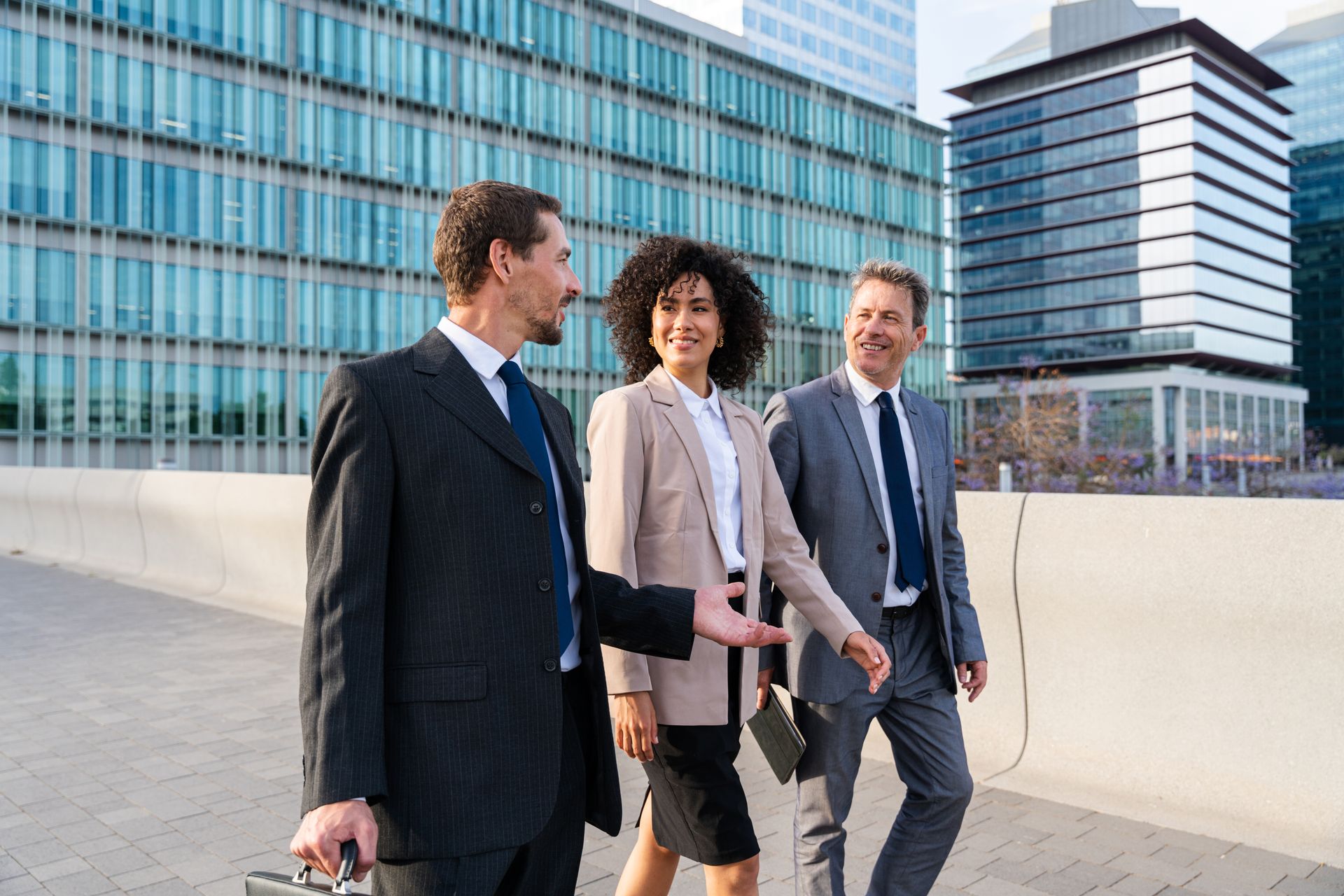 Three business people walking outdoors beside modern office buildings