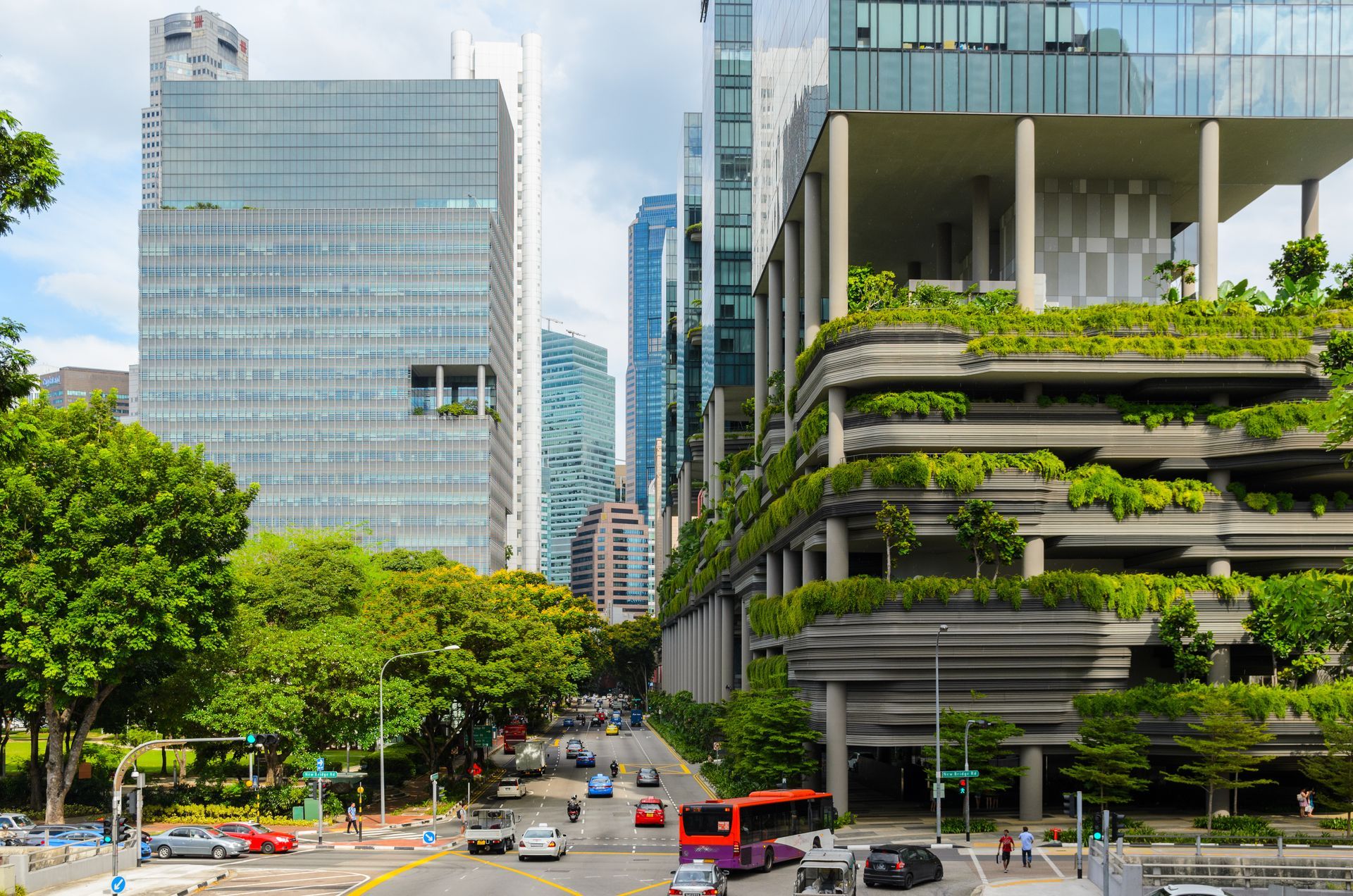 Modern city street beside glass skyscrapers and a tiered green building under a bright sky