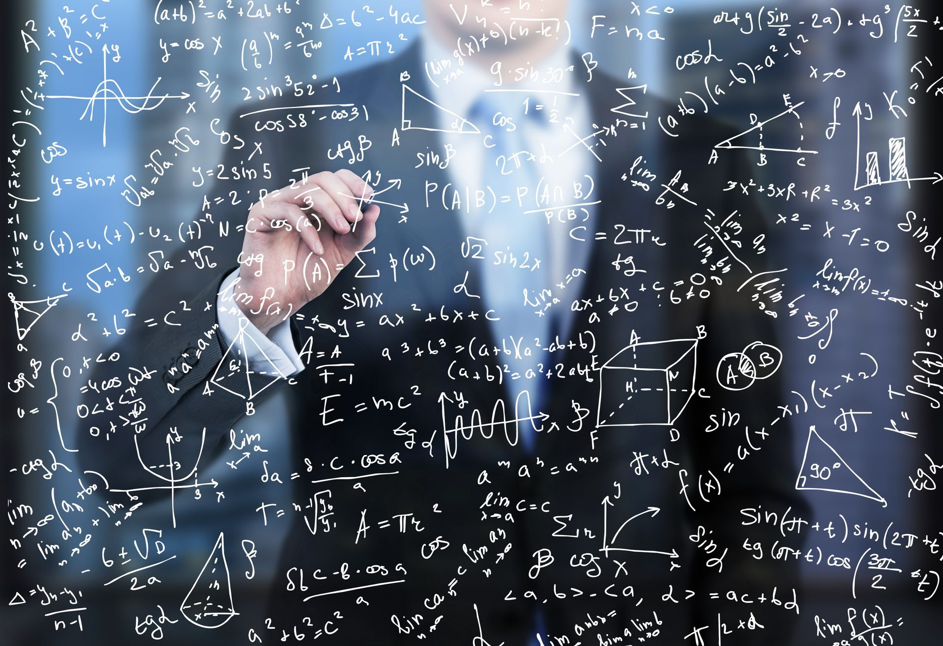 A man in a suit is writing on a blackboard with mathematical equations.