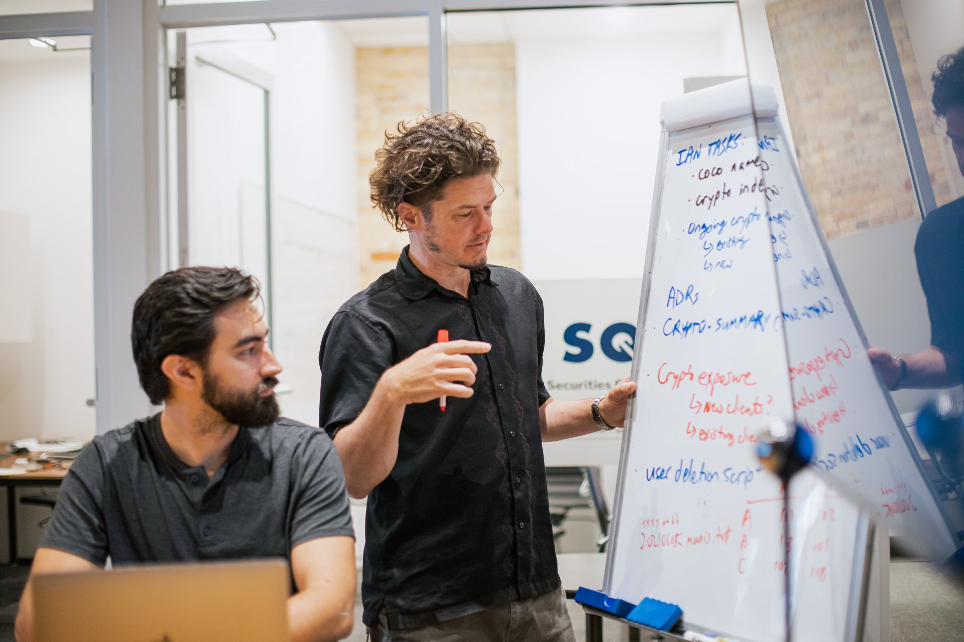 Two men are standing next to each other in front of a whiteboard.