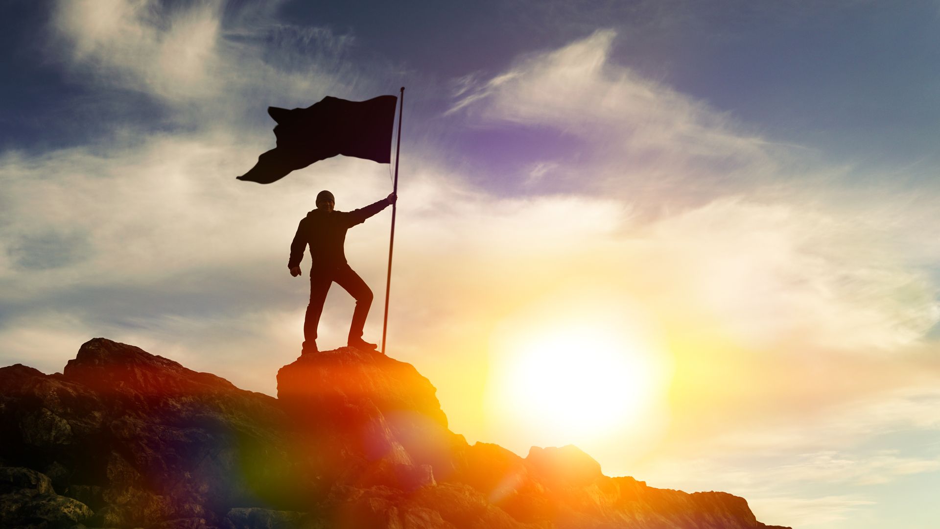 A man is standing on top of a mountain holding a flag.