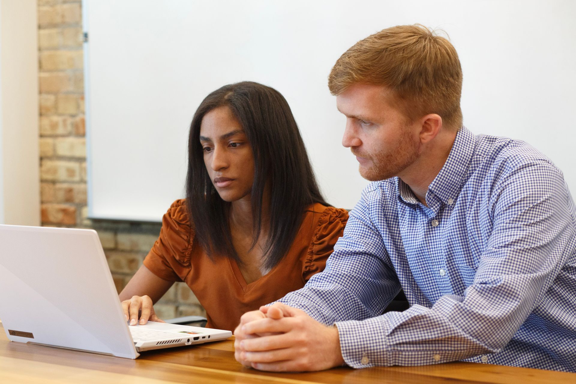 A man and a woman are sitting at a table looking at a laptop computer.
