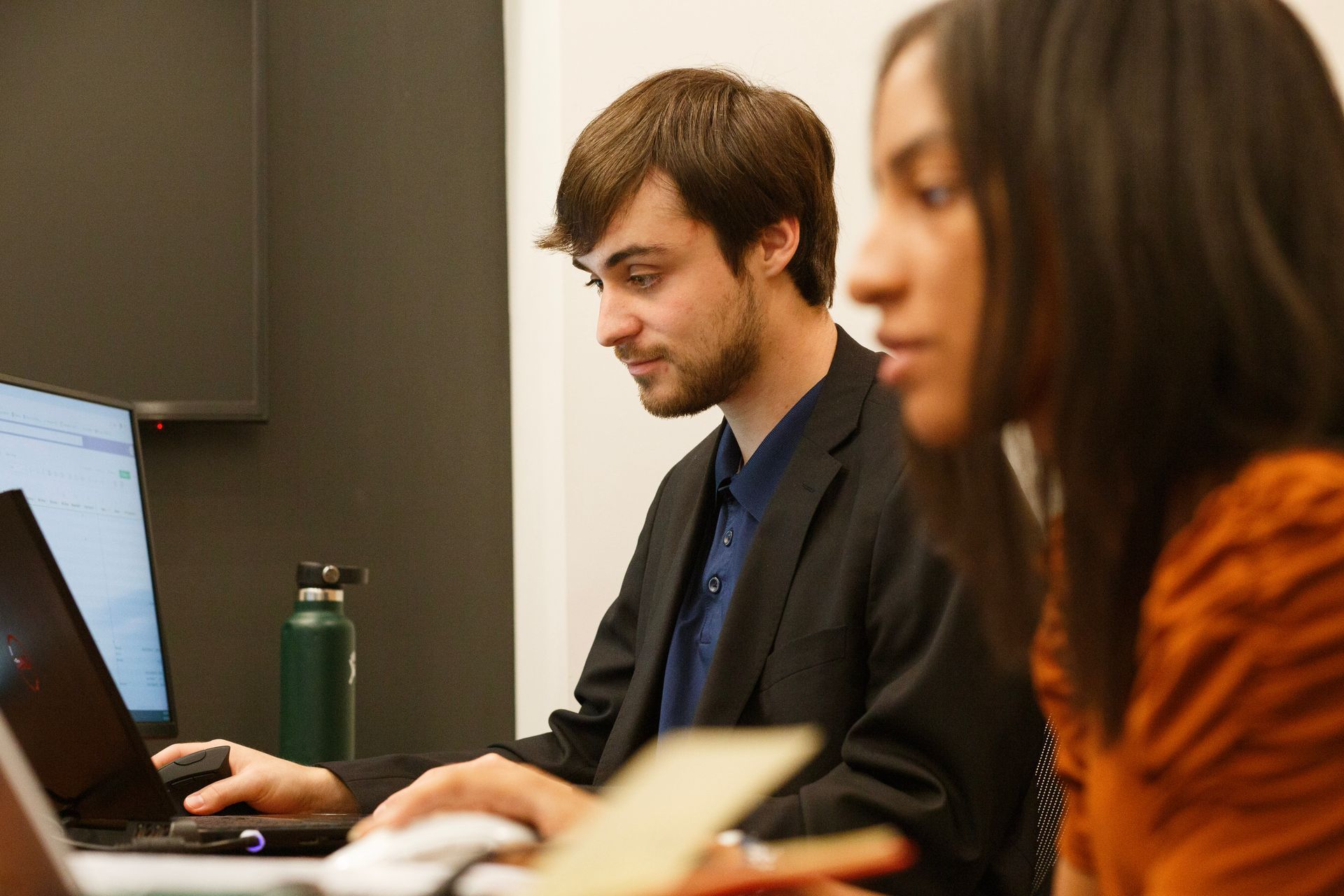 A man and a woman are sitting at a table using laptops.
