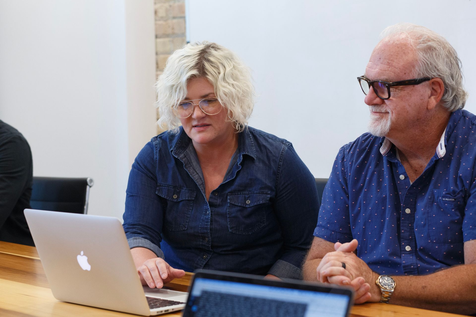 A man and a woman are sitting at a table looking at a laptop.