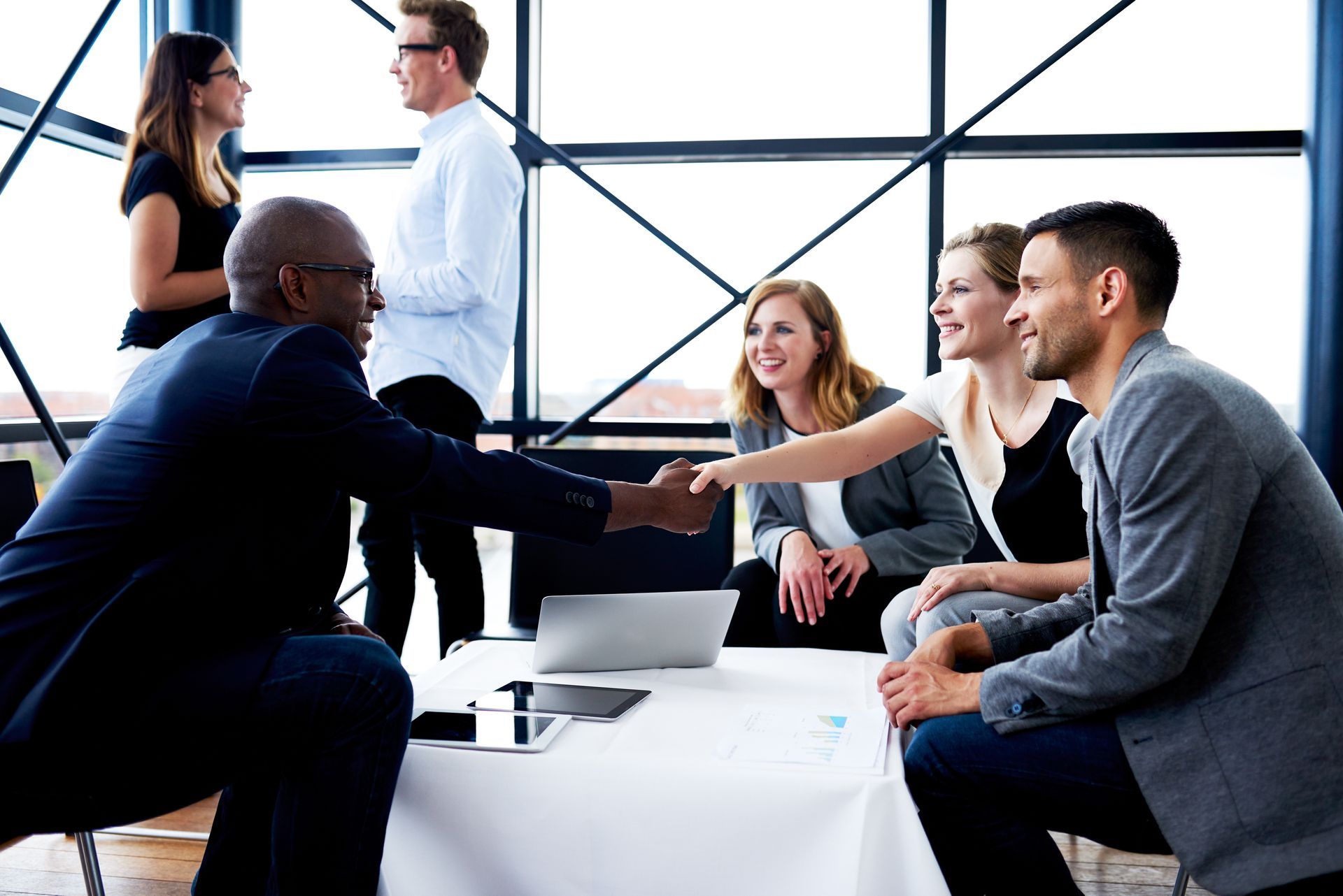 A group of people are sitting around a table shaking hands.