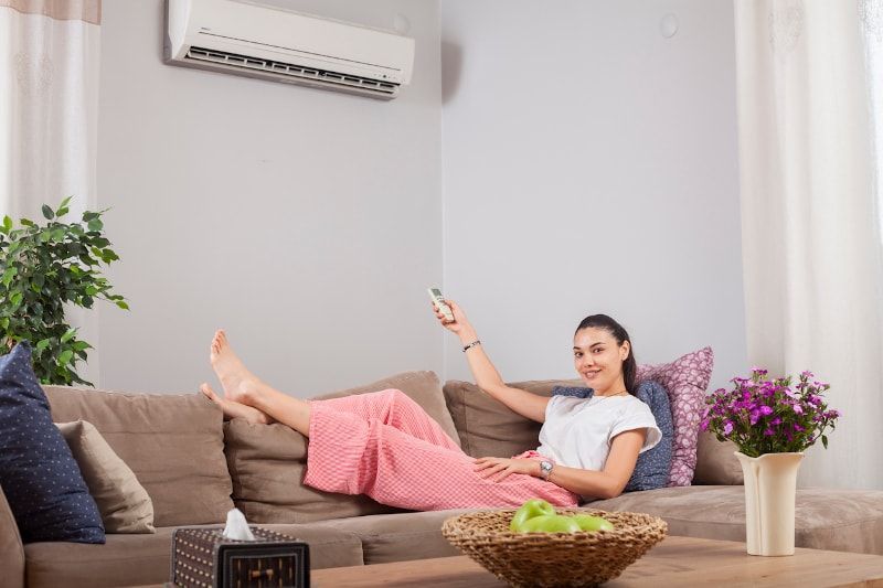 Woman relaxing on couch, using AC remote