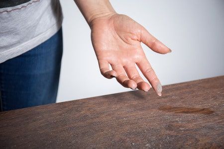 Hand reaching down to touch a wet spot on a wooden surface Hand reaching down to touch a wet spot on a wooden surface