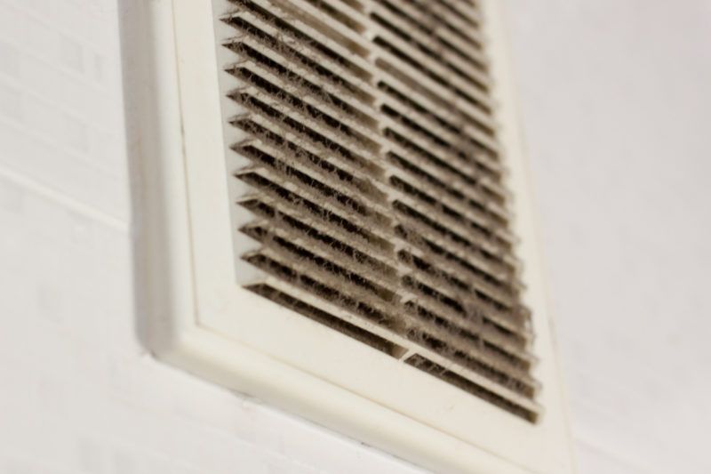 Dirty, white air vent with dust buildup on a white wall Dirty, white air vent with dust buildup on a white wall