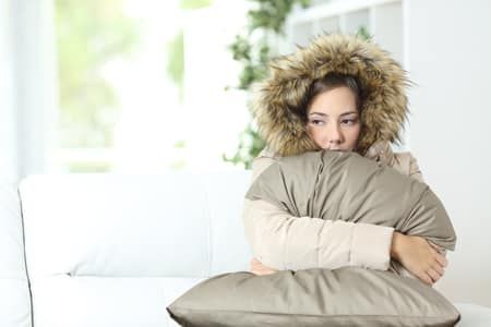 Woman bundled in winter coat and hood sits on a couch