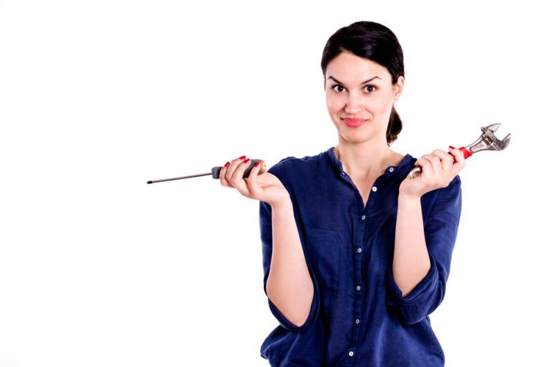 Woman in blue shirt holding a screwdriver and a wrench Woman in blue shirt holding a screwdriver and a wrench