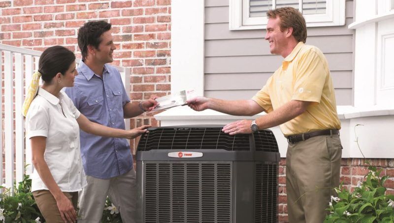 Man handing paperwork to a couple next to an outdoor HVAC unit