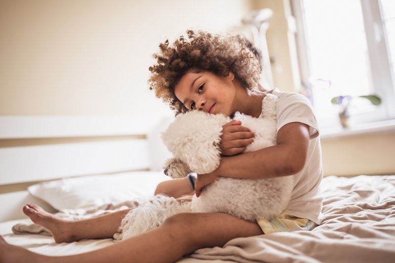 Young person with curly hair hugs a fluffy white dog
