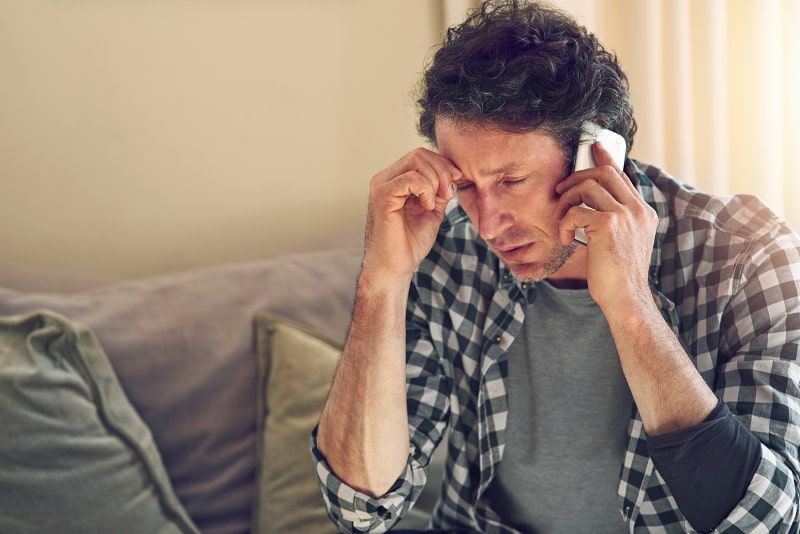 Man on phone, looking stressed, sitting on a couch Man on phone, looking stressed, sitting on a couch